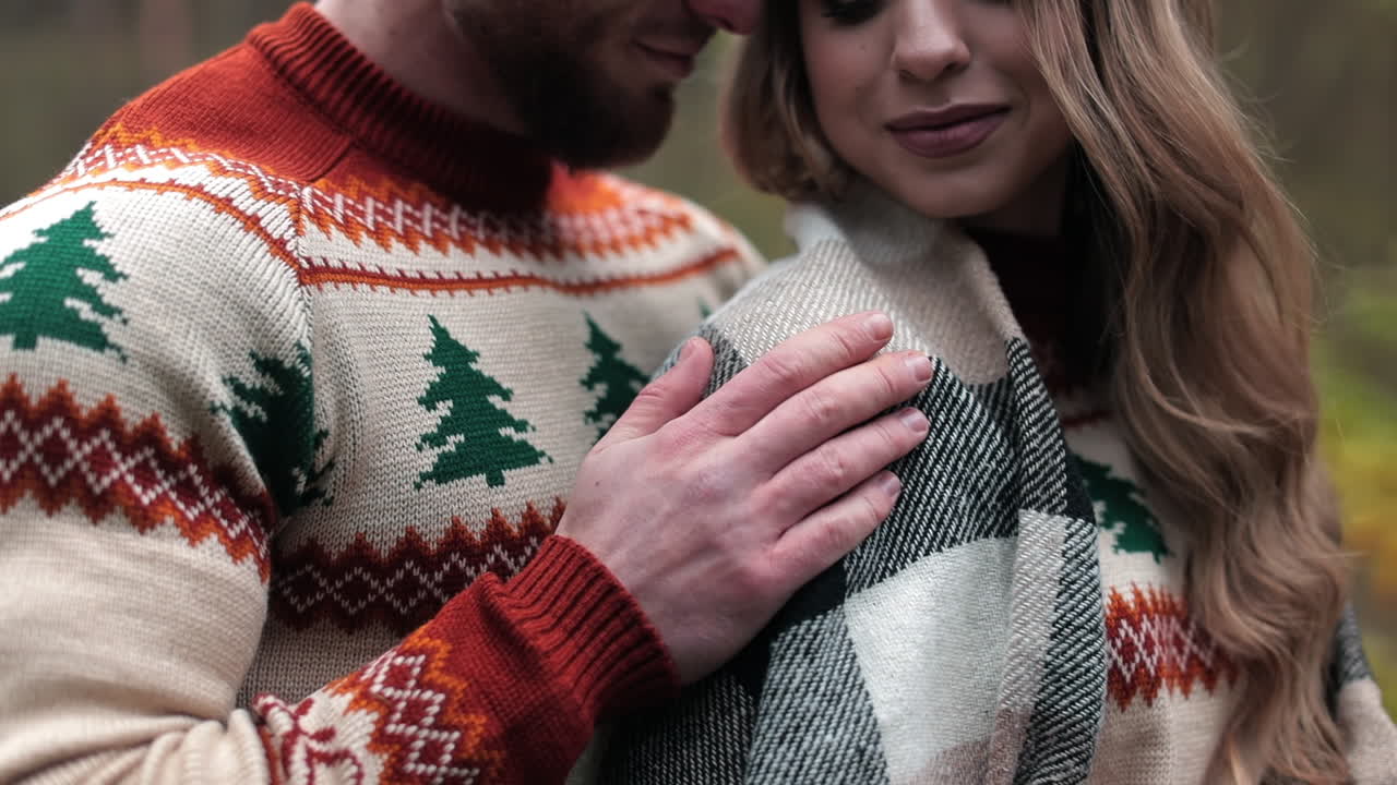 Happy couple wearing identical sweaters enjoying their date. Man caressing his girlfriend covered with plaid. Dating couple at the nature backdrop.