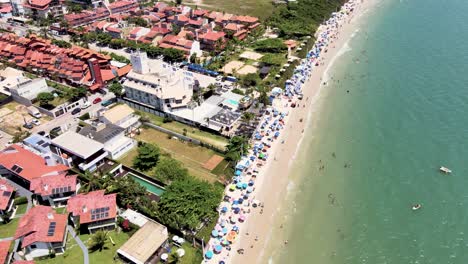 Escena-Aérea-De-Drones-De-Playa-Turística-Con-Muchas-Casas-De-Verano-Hoteles-Frente-Al-Mar-Malla-De-Playa-Urbana-Con-Mucha-Gente-Disfrutando-Del-Sol-La-Arena-Y-El-Mar-Brasil-Santa-Catarina-Jurere-Internacional