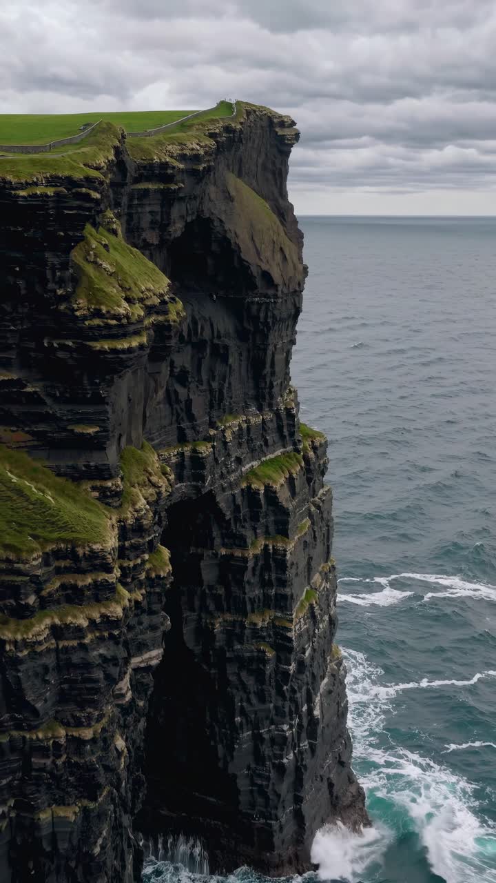 Dramatic aerial view of rugged cliffs meeting the ocean under a cloudy sky, perfect for a nature