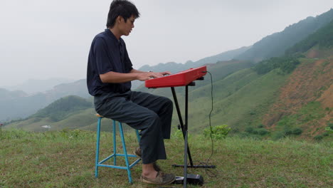 concentrated young asian guy playing electronic piano on top of a hill