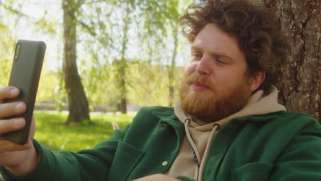 man with beard taking a selfie or making a video call in a park