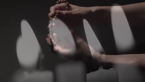 burning candles against hands holding christian rosary and praying