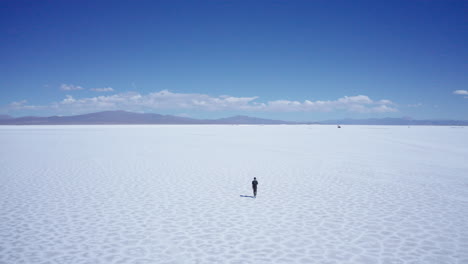 Lone-unrecognizable-man-walks-at-vast-salt-flats-in-Argentina,-aerial