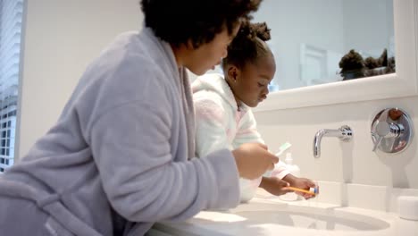 african american mother and daughter rinsing toothbrushes in bathroom, slow motion