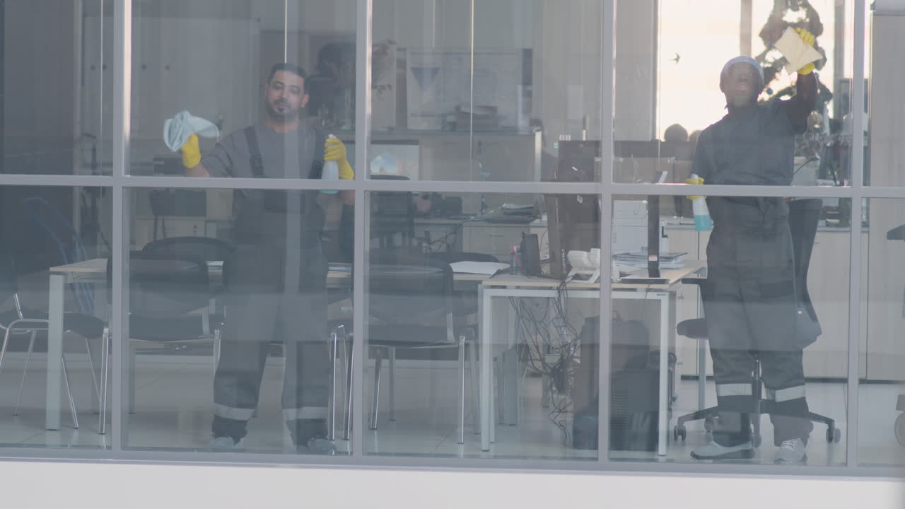 vista desde el exterior y un hombre de limpieza árabe limpiando los cristales de las ventanas dentro de una oficina 2