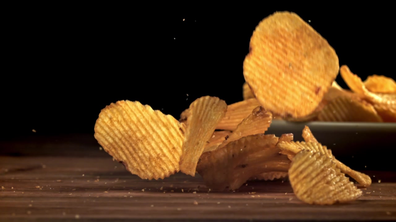 Patatine fritte croccanti in caduta al rallentatore su una superficie di legno