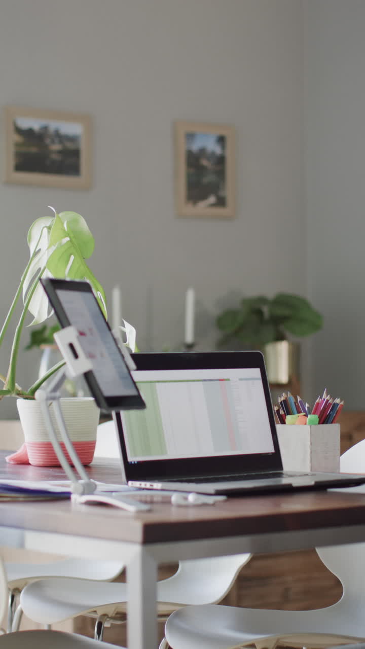 Video vertical de una habitación de casa con una computadora portátil y una tableta con gráficos en las pantallas sobre una mesa, en cámara lenta.
