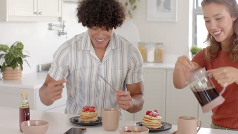 young diverse couple enjoying pancakes with strawberries and coffee in modern kitchen, at home