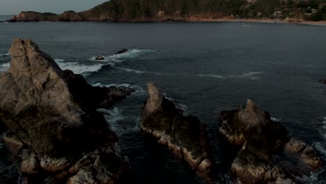 Rotierende-Luftaufnahme-über-Einer-Kleinen-Felsigen-Insel-In-Der-Nähe-Von-Mazunte-Beach,-Oaxaca,-Mexiko-Mit-Wellen,-Die-Bei-Sonnenuntergang-Auf-Der-Insel-Zusammenbrechen