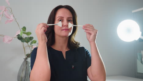 portrait view of joyful skin expert playfully posing with two silicone facial brushes under ring light in stylish spa setting, radiating confidence and fun in modern bright treatment room