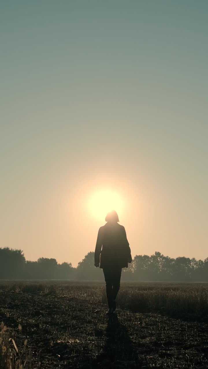 Sagoma di una persona che cammina verso l'alba in un campo