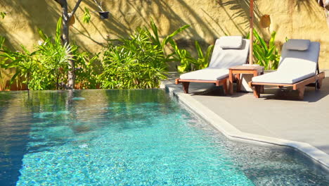 luxury lounge area for a couple rest with two deck chairs and umbrella next to the swimming pool surrounded with green plants background