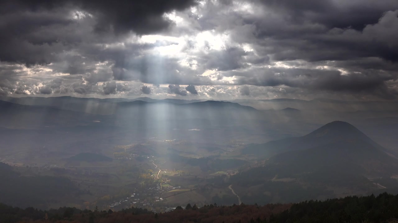 Raggi di sole drammatici che filtrano attraverso nuvole temporalesche su una valle di montagna