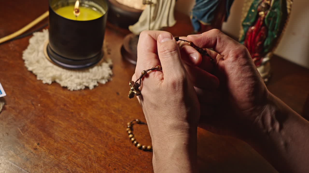 Hands Praying with Rosary Beads by Candlelight