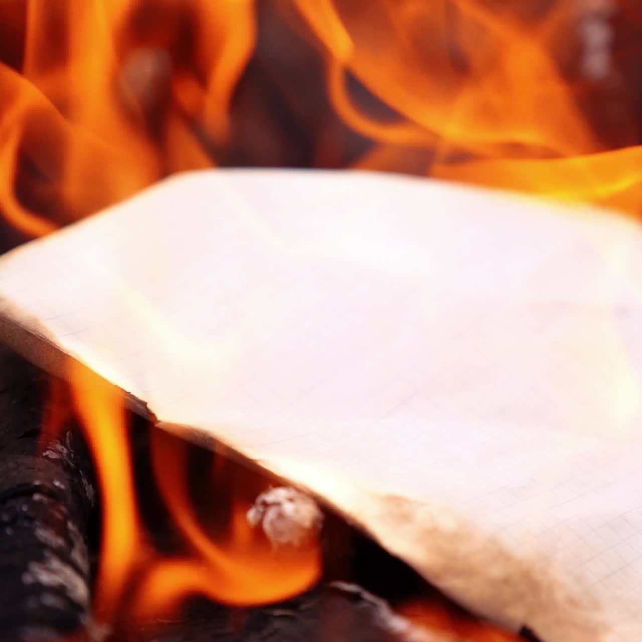 Paper is falling to the fire. Notebook sheet inflames immediatly. Red flames. Selective focus. Video