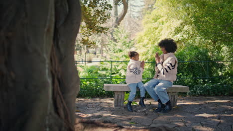 family playing patty cake sitting park bench at weekend. mom with girl