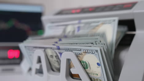 a wad of one hundred dollar bills being counted in cash machine. apparatus for counting money blurred close up.