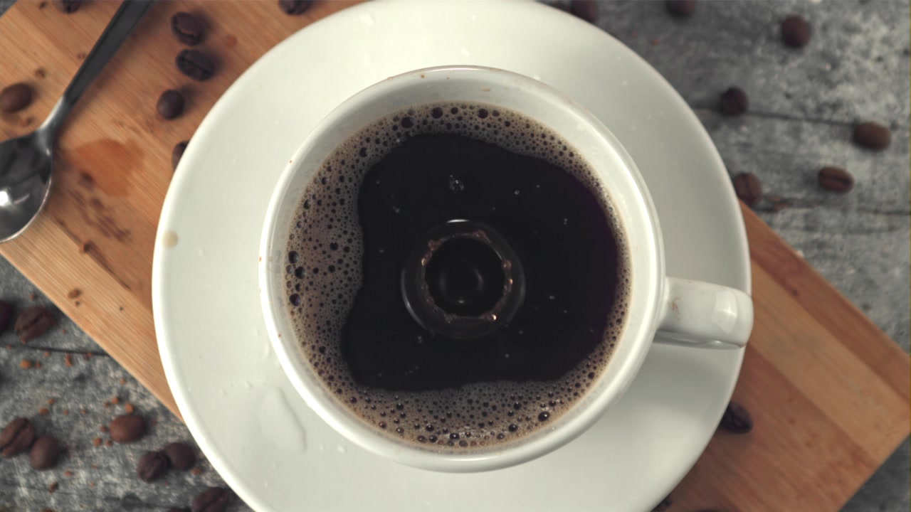 Goccia che schizza in una tazza di caffè nero caldo al rallentatore