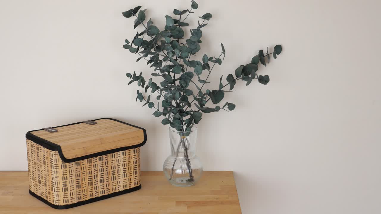 Eucalyptus in a vase next to a basket on a table