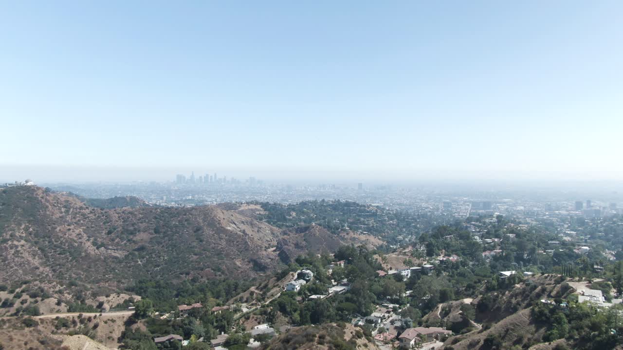 una antena en movimiento hacia adelante a gran altura sobre la colina de hollywood que supervisa un paisaje brumoso con los angeles en la lejanía