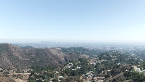 a high altitude forward moving aerial over hollywood hill overseeing a hazy landscape with los angeles in the far distance