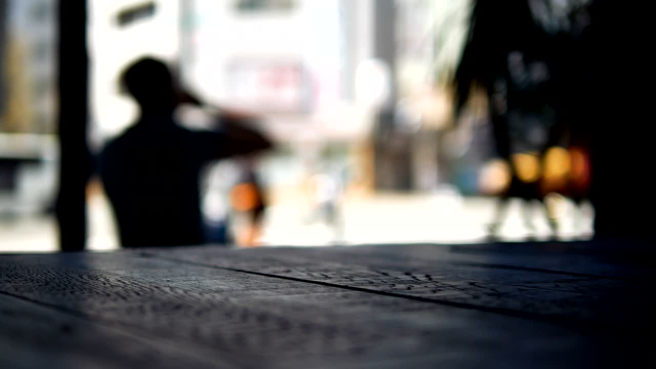 Filmato con sfondo sfocato di un uomo che prende un caffè e si siede davanti a una caffetteria, con un tavolo di legno in primo piano.