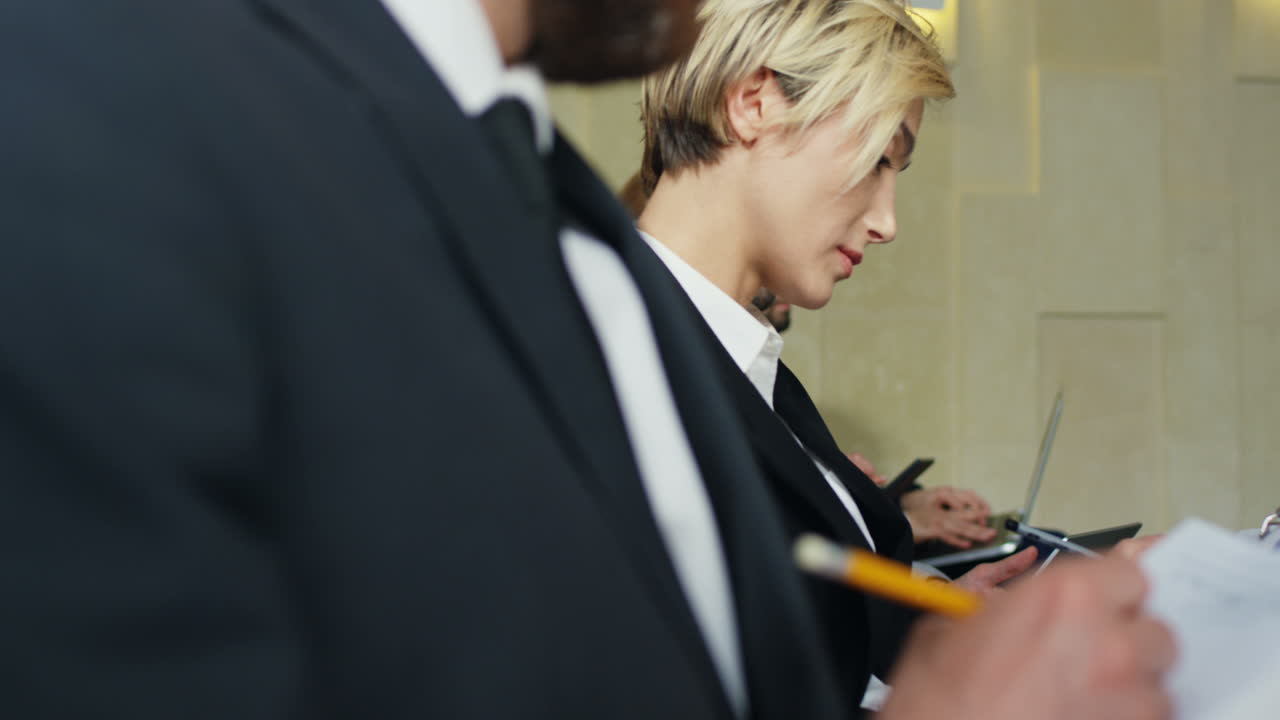 крупным планом вид многонациональных деловых людей, сидящих на стульях в конференц-зале и печатающих на ноутбуках и планшетах, слушая при этом