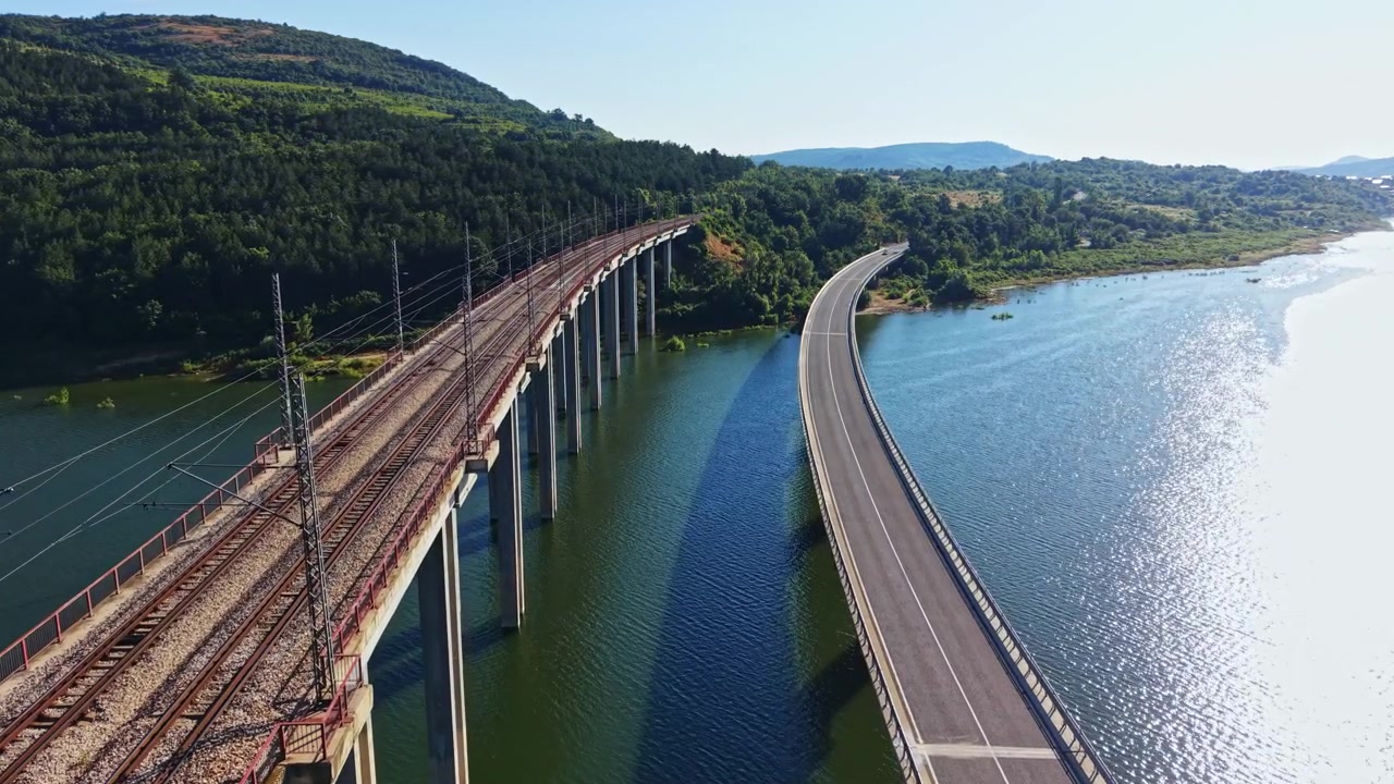 Una vista di un ponte e una strada sull'acqua circondati da verdi colline in una giornata di sole.