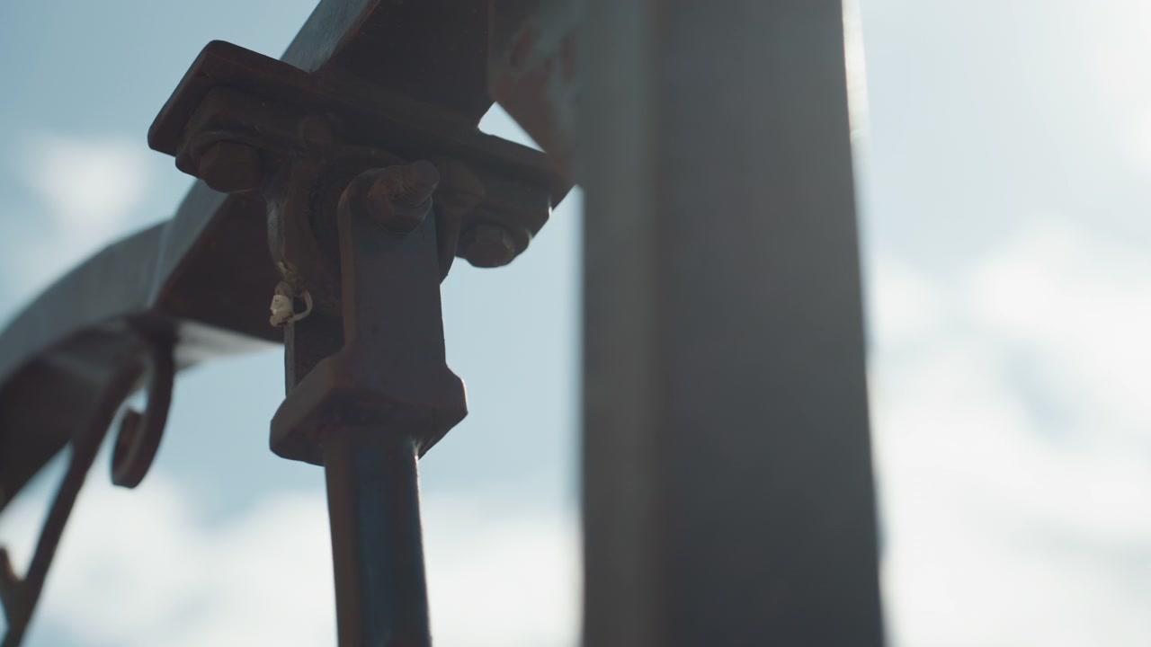 Close up of metal bracket with bolts and rusted details showing structural components in focus against out of focus sky background. scene highlights texture detail on industrial hardware