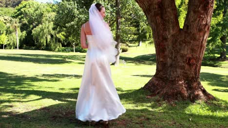 Excited-bride-holding-a-bouquet-in-the-park-smiling-at-camera