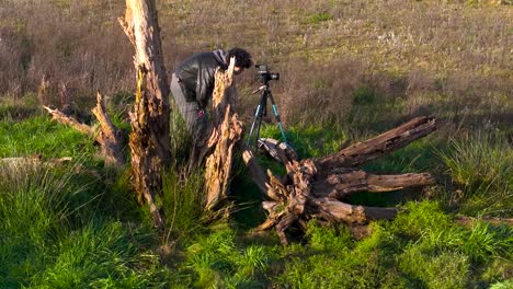 Vista-Aérea-De-Un-Fotógrafo-Masculino-Revisando-Su-Toma-En-Cámara-En-Trípode