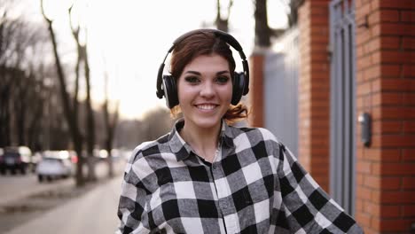 Playful,-smiling-girl-in-a-shirt-walking-on-the-street-and-moving-in-dance.-Funny-funky-style.-Headphones.-Expression.-Front-view