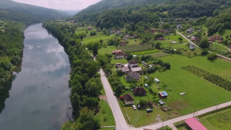 Ein-Drohnenflug-über-Eine-Malerische-Landschaft-Mit-Einem-Alten-Friedhof-Und-Einem-Fluss-Und-Einer-Hauptstraße,-Die-Seinem-Lauf-Folgt