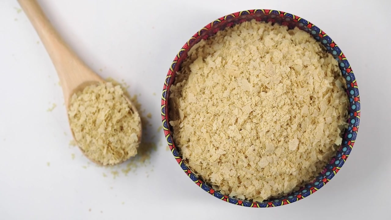 Fiocchi di lievito alimentare in una ciotola decorativa con un cucchiaio di legno.