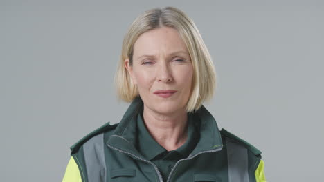 studio portrait of serious mature female paramedic against plain background