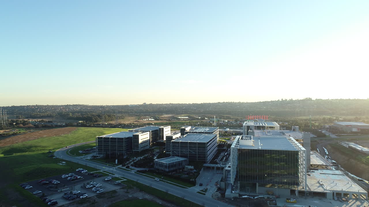 Arrow shot drone aerial perspective moving toward modern business park with car arriving at car park systematically.