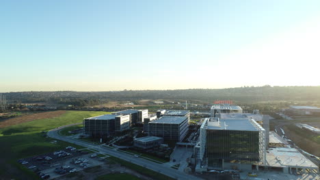 arrow shot drone aerial perspective moving toward modern business park with car arriving at car park systematically.
