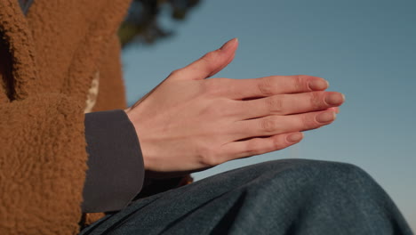 close-up shot of a person's hands gently rubbing together, indicating deep contemplation or thought. the person's face is not visible, with only jeans and a brown coat in view