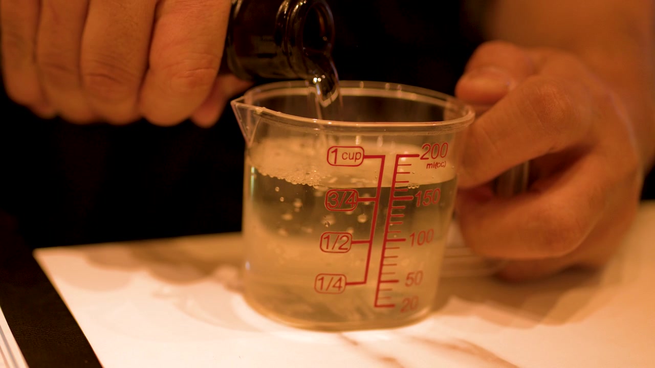 瓶からプラスチック製の計量カップに日本酒を注ぐ手のクローズアップショット