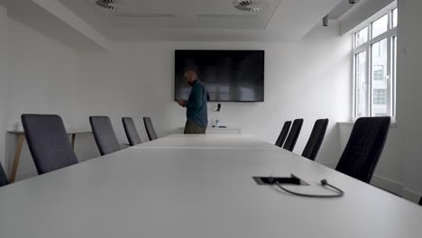 an establishing shot of a casually dressed asian man, stressed as he paces back and forth in an empty office meeting room while texting on his mobile phone