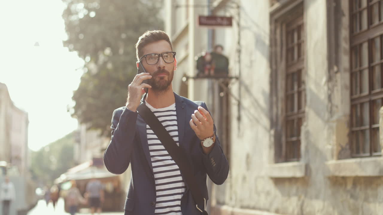 Handsome Man In Stylish Outfit And Glasses Talking On The Mobile Phone While Walking In The Old Town