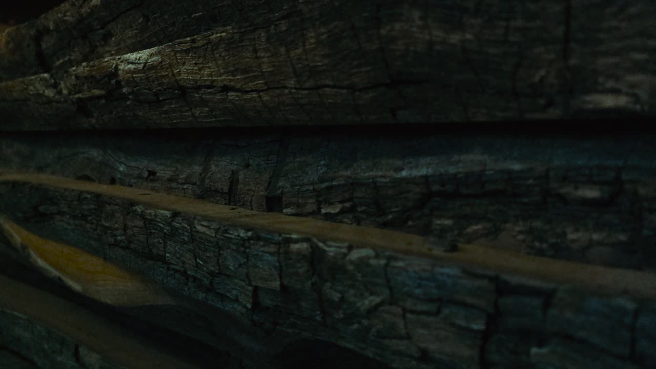 Close up tracking shot of stacked rustic oak planks. Macro sideways view reveals beautiful wood grain patterns, naturally aged rough dark bark and raw texture of cut surfaces. Layered wooden boards