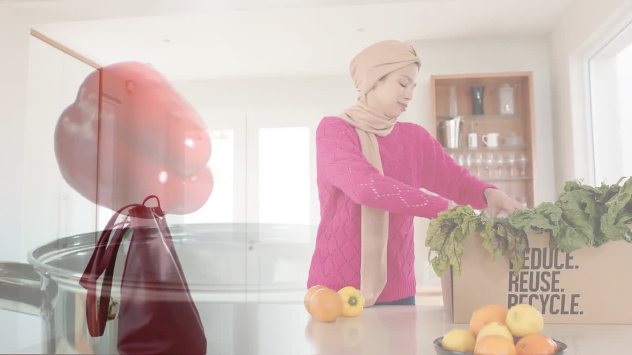 Biracial woman in hijab with box of vegetables in kitchen, cooking over red pepper