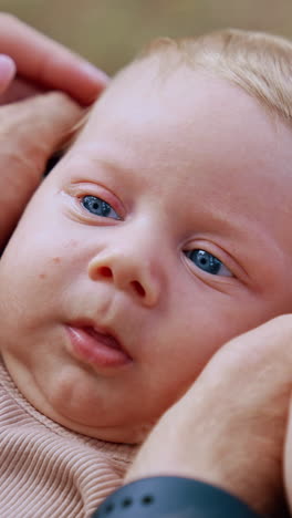 hands of parents hold the head of baby from both sides. blue-eyed blonde kid's portrait. close up. vertical video