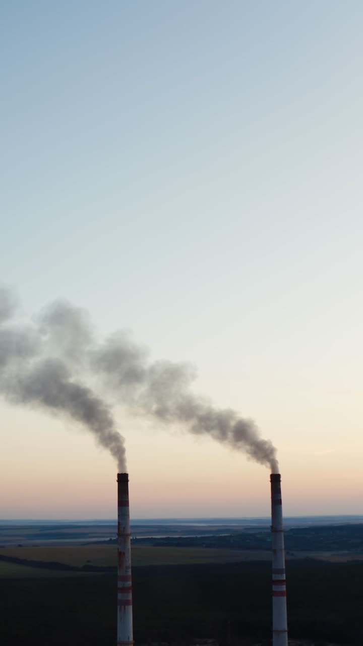 Two pipes with smoke on the fields background. Industrial pipes with smoke among fields and forests in the evening. Vertical video
