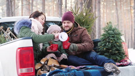 a young family of three people is drinking hot tea from a thermos sitting in the back of a car near