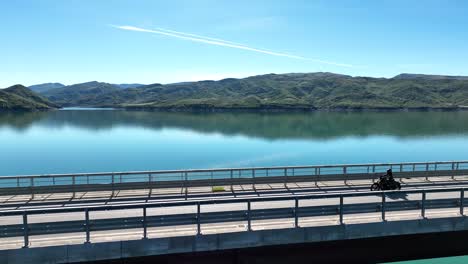 Motorcycle-chopper-travelling-across-an-empty-bridge-over-a-blue-lake