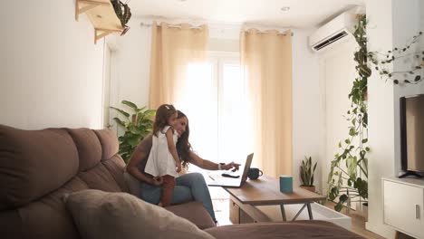 smiling mother and daughter using netbook on sofa at home
