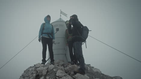 aljaž 타워 앞 triglav 산 정상에 있는 등산객들이 주위를 둘러보려 하지만 구름이 시야를 가리고 있습니다.