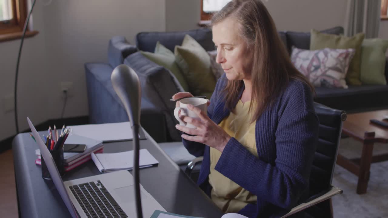 Kvinde drikker kaffe, mens hun bruger bærbar computer derhjemme